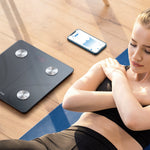 Woman exercising on a blue mat with a digital weight scale and smartphone nearby.