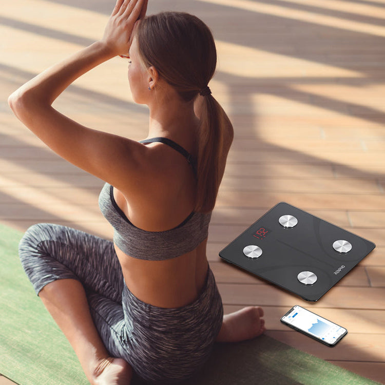 Woman sitting on a yoga mat with a RENPHO smart digital bathroom scale next to her.