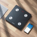 Digital weight scale on a wooden floor with a smartphone displaying app