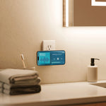 A smartphone mounted on a bathroom wall near a sink, displaying a blue music player interface. The scene includes a folded towel, toothbrush holder, soap dispenser, faucet, and warm ambient lighting in a real bathroom setting.