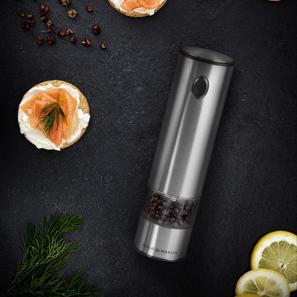 Pepper grinder with sliced lemon and pepper on a dark surface