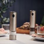 Two stainless steel salt and pepper shakers on a table with food and decor in the background.