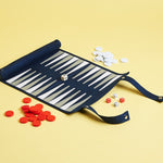A roll-up backgammon set with pieces spread out on a yellow background, including a blue foldable case with zipper compartment.